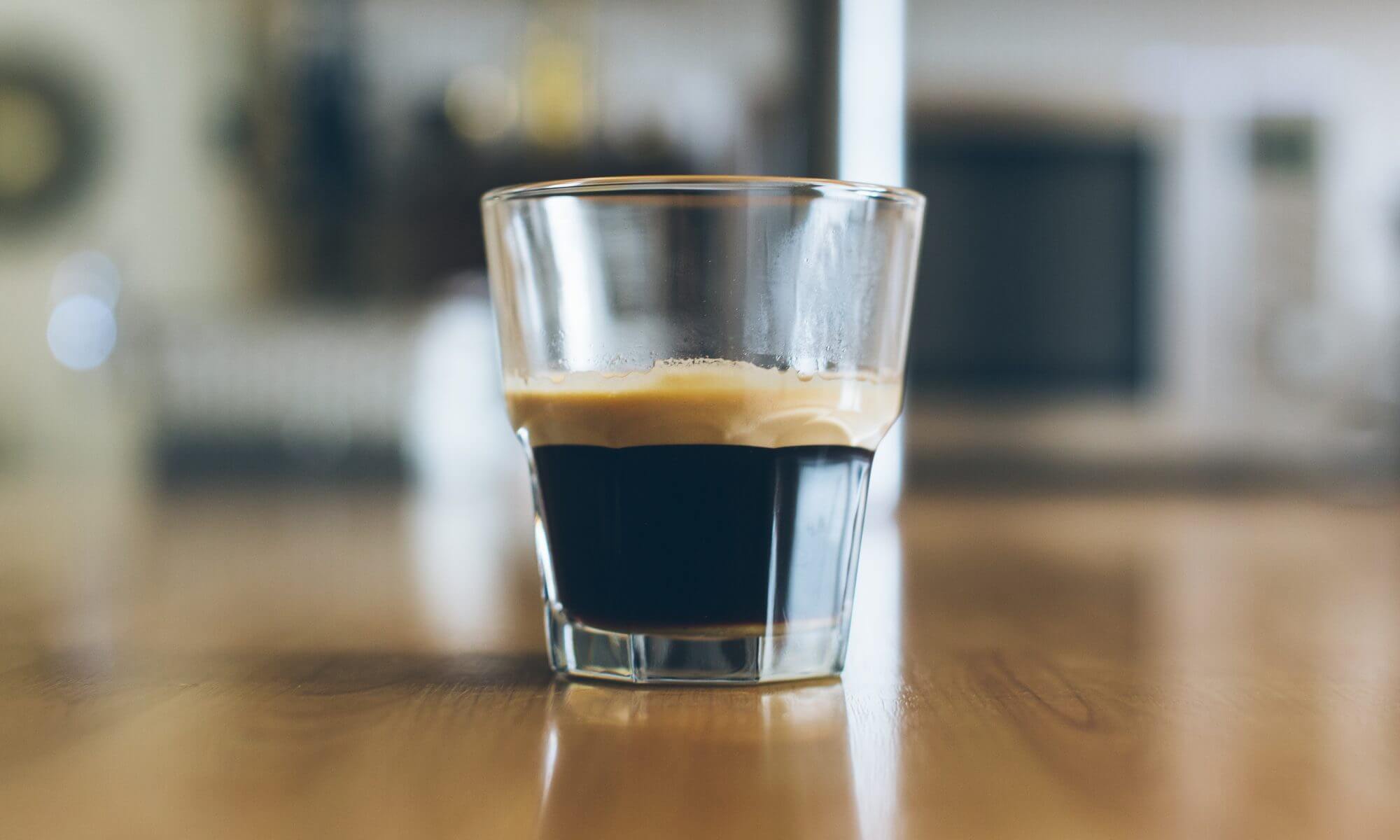 Espresso-Glas auf einem Holztisch in ruhiger Coworking-Umgebung